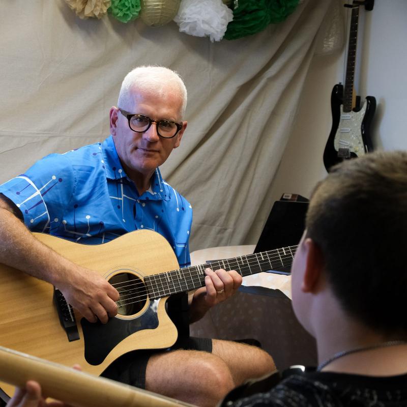 Steve Zaat playing acoustic guitar during a lesson with a student at the Creative Rebel art studio